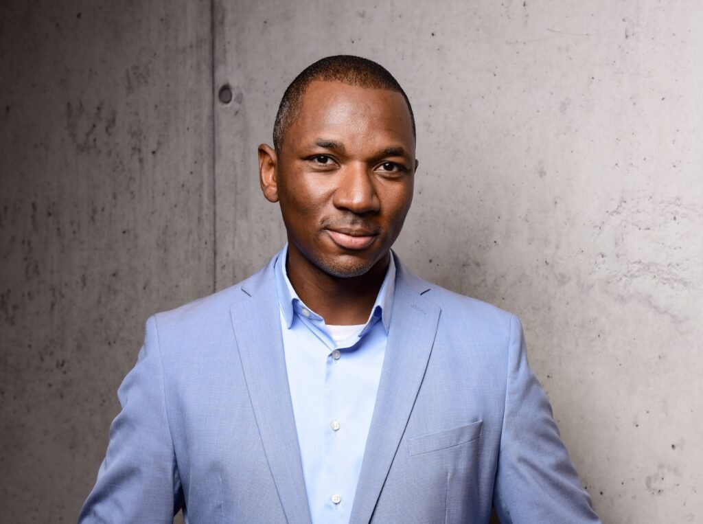 Jean A. Boni, founder and AI visionary of Smainos, in a light blue suit against a concrete background